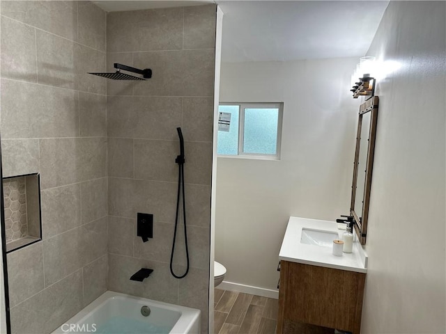 bathroom with baseboards, wood finish floors, toilet, vanity, and  shower combination