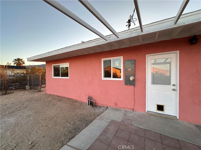 property entrance with stucco siding, a patio area, and fence