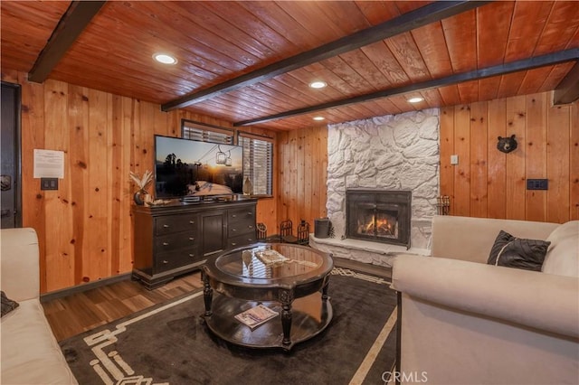 living area with beam ceiling, a stone fireplace, wooden ceiling, and wood finished floors