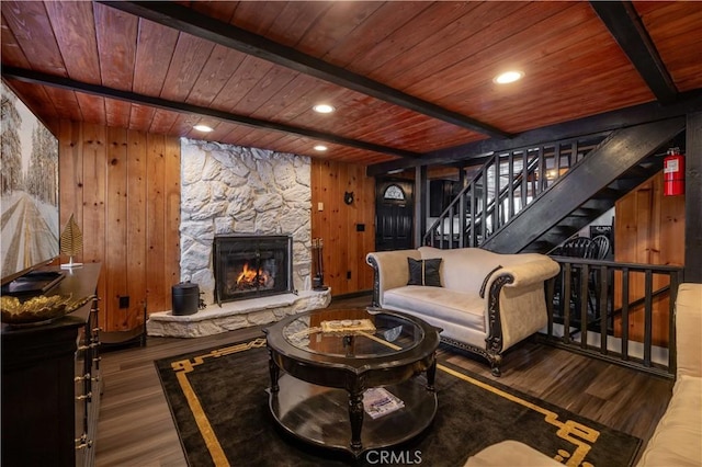 sitting room with a stone fireplace, stairway, beamed ceiling, and wood finished floors