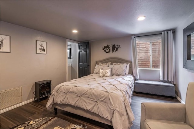 bedroom featuring visible vents, baseboards, recessed lighting, a wood stove, and wood finished floors