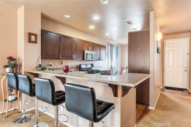 kitchen with a kitchen bar, visible vents, stainless steel appliances, carpet, and light countertops