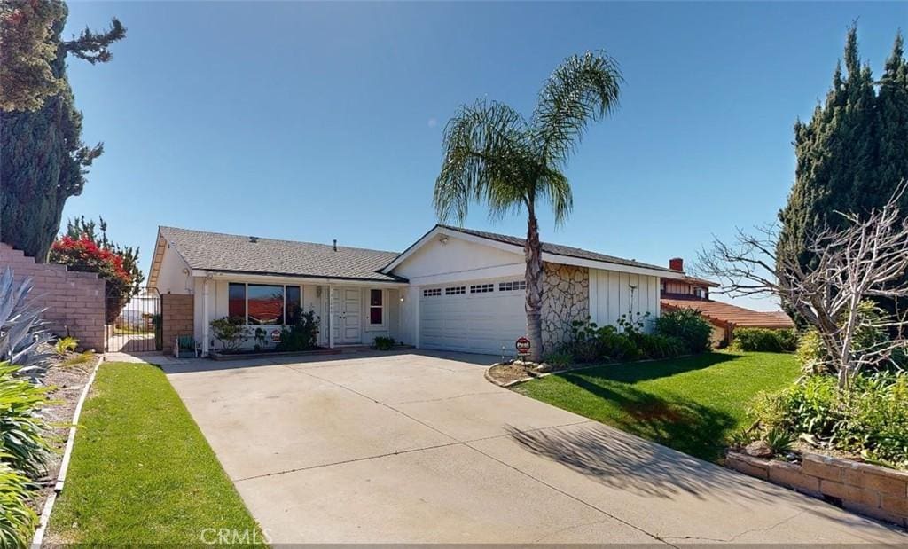 ranch-style home featuring fence, concrete driveway, a front yard, an attached garage, and a gate