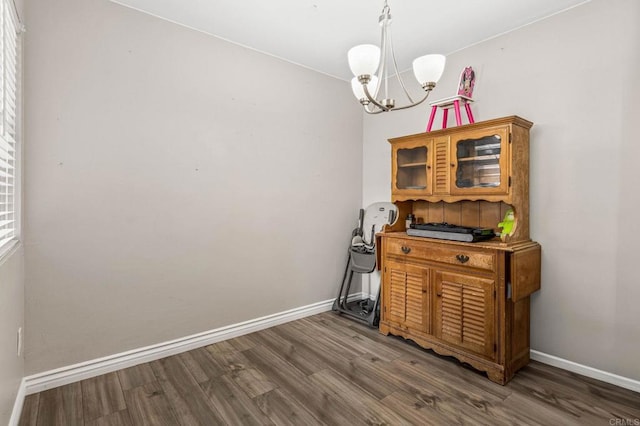 dining area with dark wood-type flooring, a notable chandelier, and baseboards