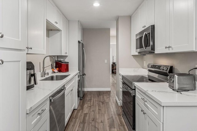 kitchen with baseboards, stainless steel appliances, wood finished floors, white cabinetry, and a sink