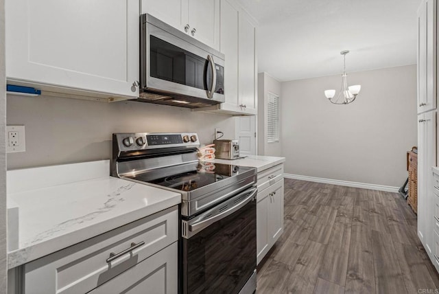 kitchen with wood finished floors, baseboards, stainless steel appliances, white cabinetry, and a notable chandelier