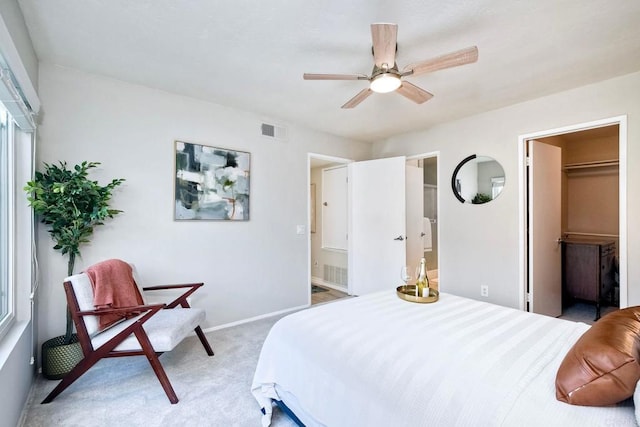 bedroom with visible vents, baseboards, ensuite bathroom, a walk in closet, and light colored carpet