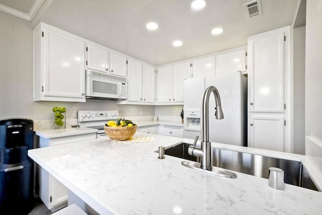 kitchen with light stone counters, white appliances, white cabinets, and recessed lighting