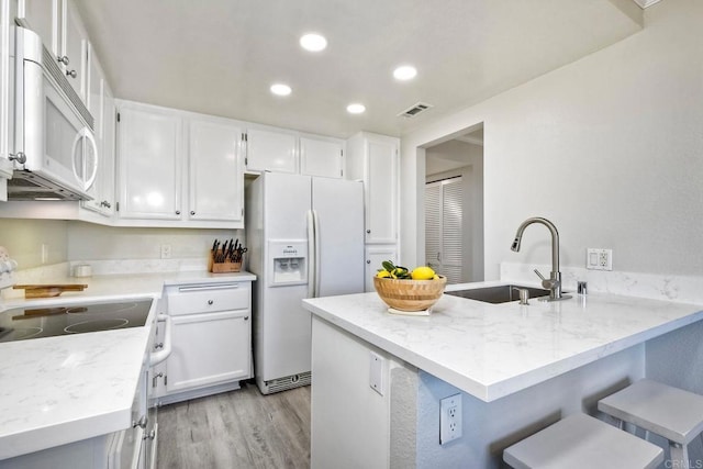 kitchen featuring white appliances, light stone counters, visible vents, a peninsula, and a sink