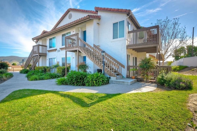 rear view of property with a tiled roof, stairway, a yard, and stucco siding