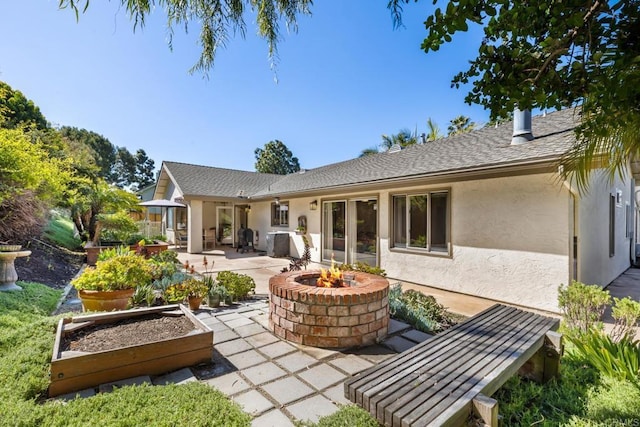 rear view of property with a garden, stucco siding, an outdoor fire pit, and a patio area