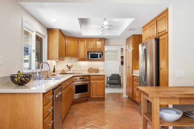 kitchen featuring brown cabinets, a sink, a tray ceiling, stainless steel appliances, and light countertops