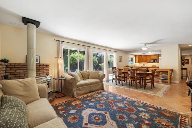 living room featuring light tile patterned floors, baseboards, ceiling fan, and a wood stove