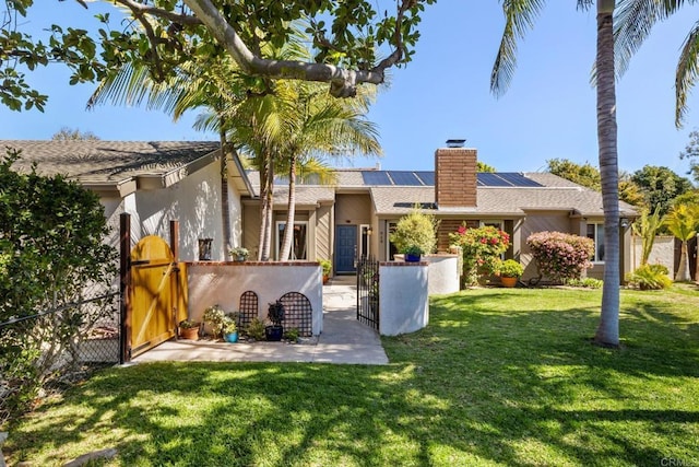 view of front of property with a front yard, a gate, fence, a chimney, and roof mounted solar panels