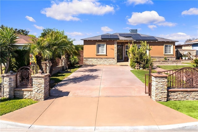 view of front of home with solar panels, fence, stone siding, and stucco siding