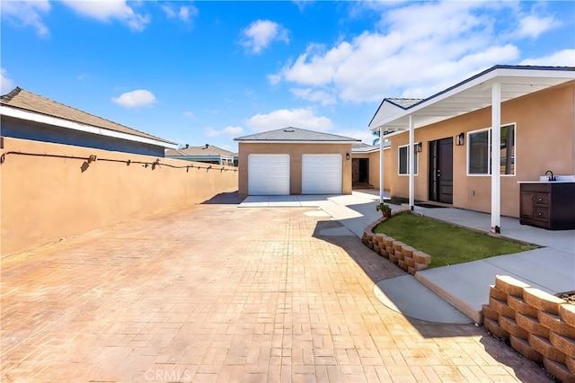 exterior space featuring fence, driveway, a sink, an outdoor structure, and a garage