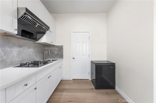 kitchen featuring under cabinet range hood, stainless steel gas cooktop, white cabinetry, fridge, and a sink