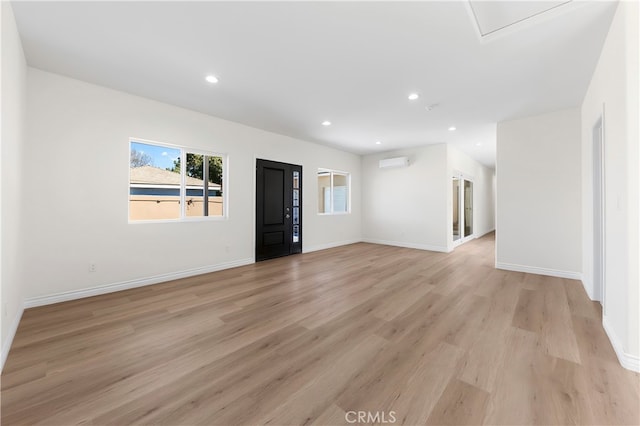 spare room featuring an AC wall unit, recessed lighting, light wood-type flooring, and baseboards