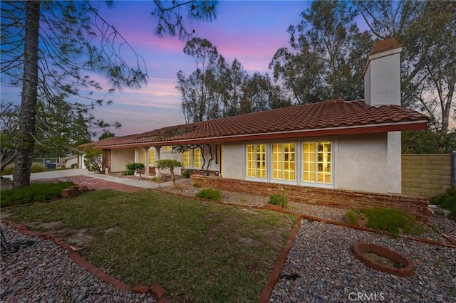 view of front of home with a chimney, stucco siding, a tiled roof, a lawn, and brick siding