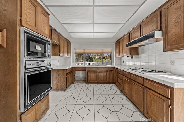 kitchen with white gas cooktop, brown cabinetry, under cabinet range hood, black microwave, and backsplash