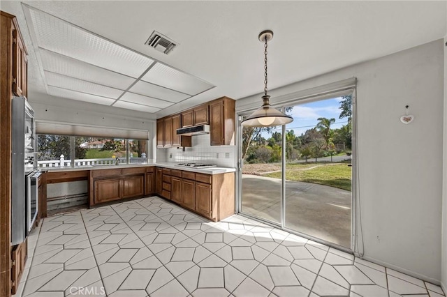 kitchen with a wealth of natural light, visible vents, under cabinet range hood, light countertops, and hanging light fixtures