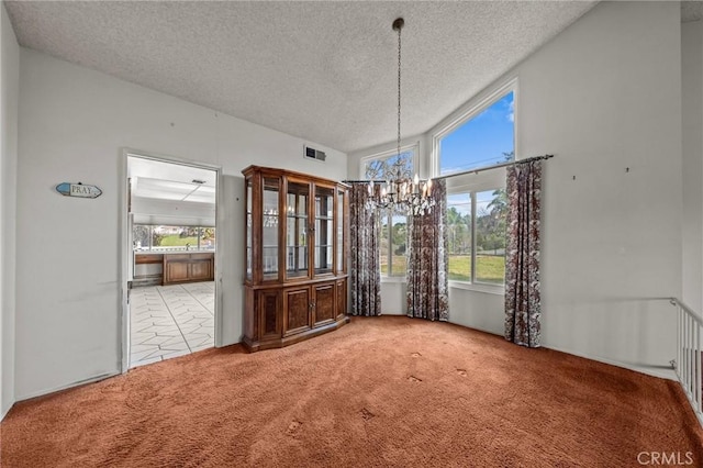 unfurnished dining area with an inviting chandelier, carpet flooring, visible vents, and a textured ceiling