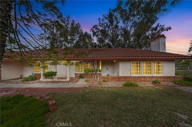 ranch-style home with stucco siding, brick siding, a chimney, and a front yard