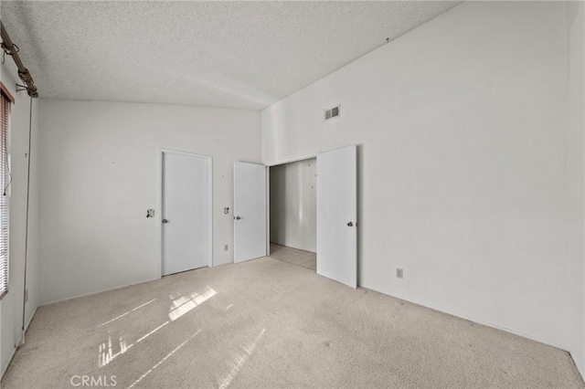 unfurnished bedroom featuring visible vents, carpet flooring, a textured ceiling, and lofted ceiling