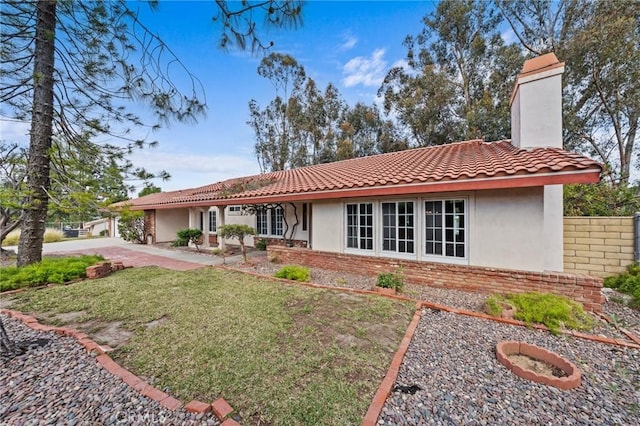 view of front facade with stucco siding, a front lawn, brick siding, a chimney, and a tiled roof