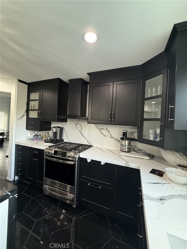 kitchen featuring stainless steel gas stove, wall chimney exhaust hood, glass insert cabinets, and dark cabinetry