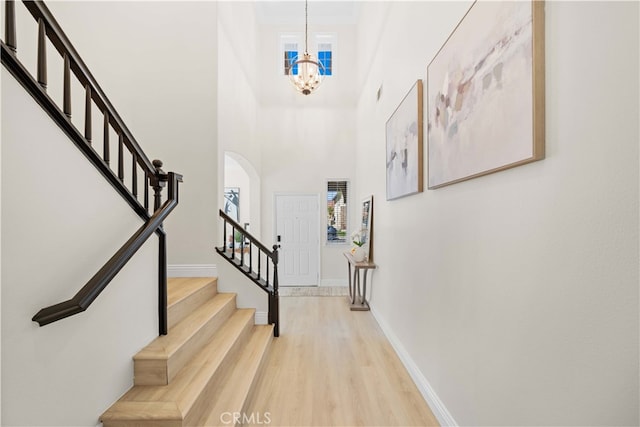 foyer with a high ceiling, baseboards, light wood-type flooring, and a chandelier