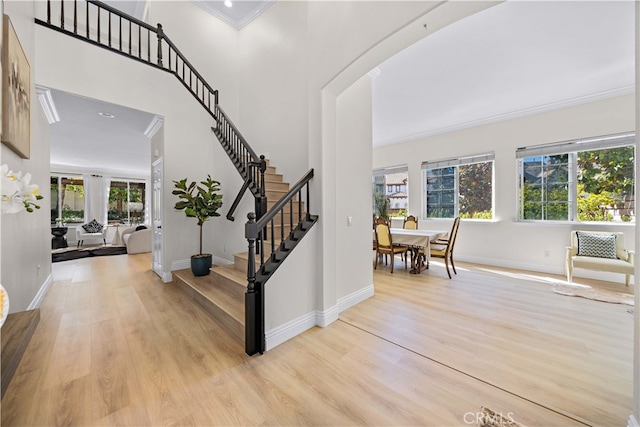 entryway featuring baseboards, light wood finished floors, a high ceiling, ornamental molding, and stairs