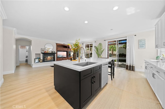 kitchen with dark cabinetry, a sink, light countertops, dishwasher, and a glass covered fireplace