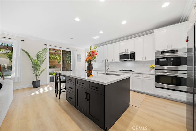 kitchen with light wood-style flooring, a sink, backsplash, white cabinetry, and stainless steel appliances