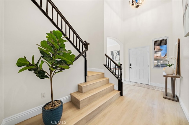 foyer featuring baseboards, stairs, a high ceiling, light wood-style floors, and arched walkways