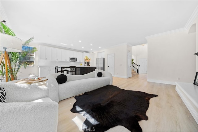 living area featuring baseboards, light wood-style flooring, ornamental molding, stairs, and a glass covered fireplace