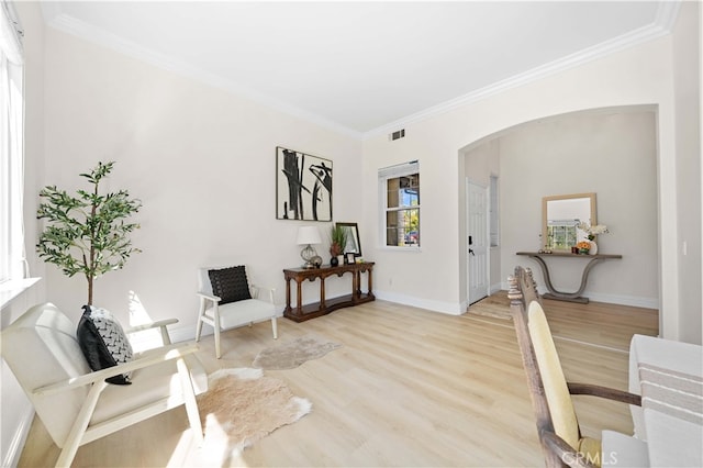 sitting room with visible vents, baseboards, ornamental molding, light wood-style floors, and arched walkways