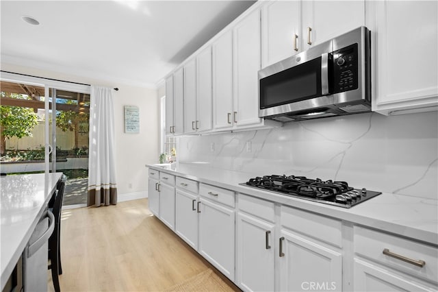 kitchen with stainless steel microwave, gas cooktop, tasteful backsplash, white cabinetry, and light wood-style floors