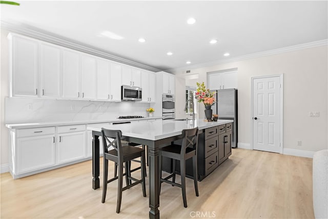 kitchen with light wood-style floors, appliances with stainless steel finishes, a center island with sink, and white cabinetry