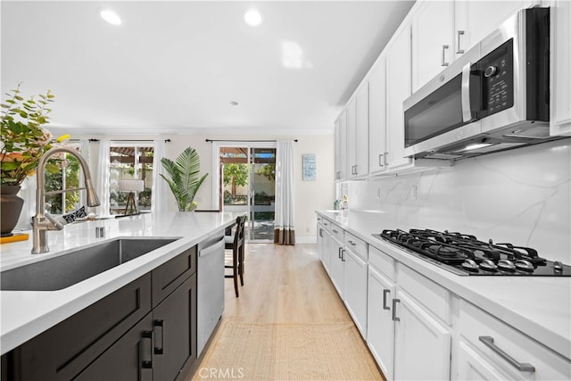 kitchen with a sink, white cabinets, backsplash, and stainless steel appliances