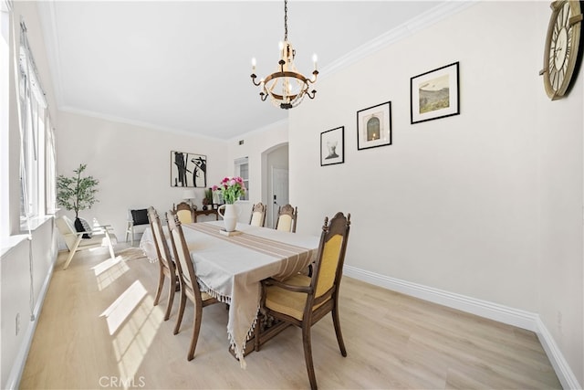 dining area featuring ornamental molding, arched walkways, light wood-style floors, an inviting chandelier, and baseboards