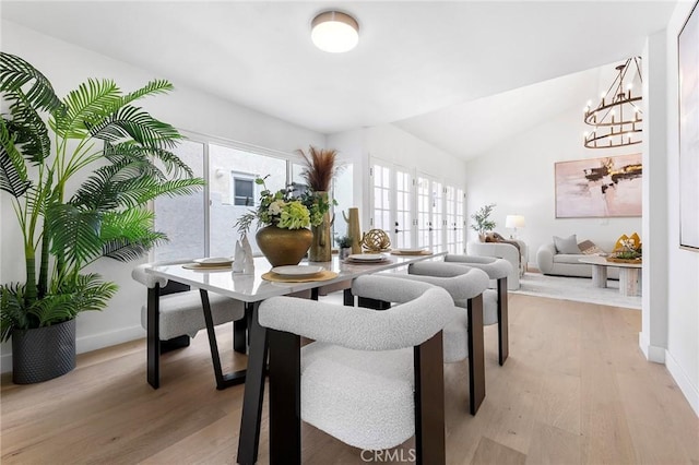 dining space featuring baseboards, lofted ceiling, light wood-style floors, and a chandelier