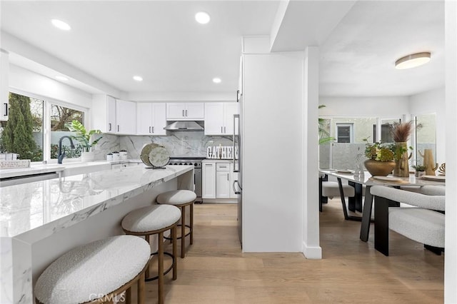 kitchen featuring under cabinet range hood, white cabinets, stainless steel range oven, and light wood-style floors