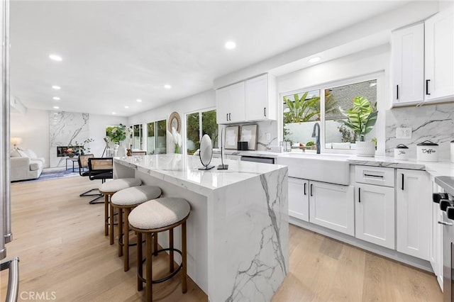 kitchen with a kitchen bar, light wood-style flooring, a sink, light stone counters, and a center island