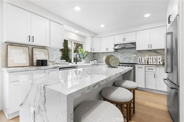 kitchen featuring a breakfast bar, a sink, stainless steel appliances, under cabinet range hood, and white cabinetry