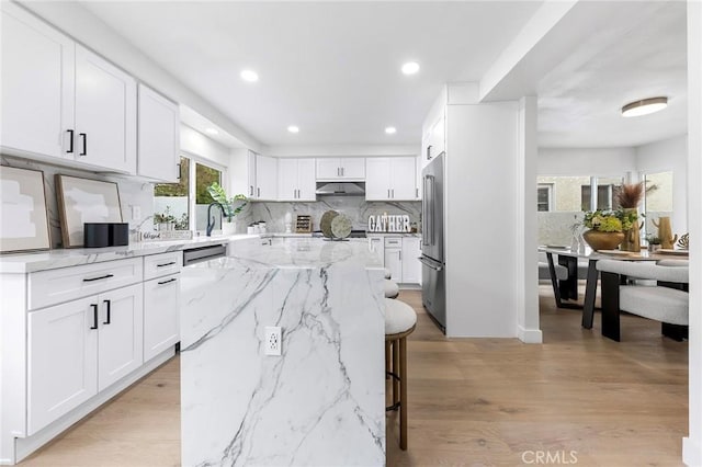 kitchen with under cabinet range hood, a center island, stainless steel appliances, white cabinets, and decorative backsplash