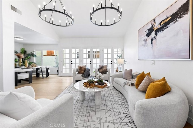 living room with wood finished floors, visible vents, an inviting chandelier, vaulted ceiling, and french doors