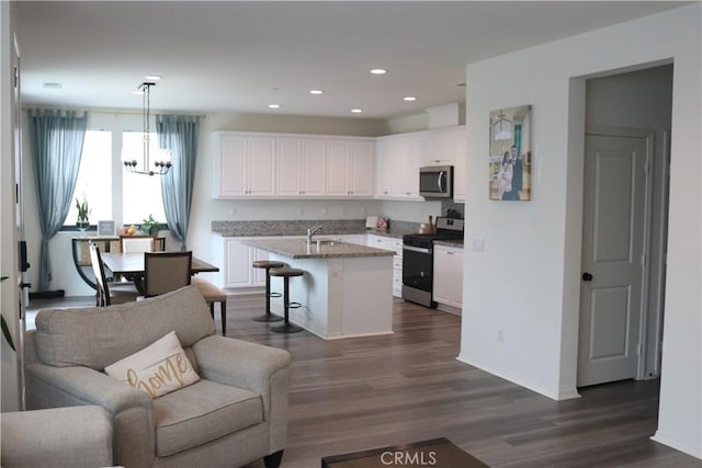 kitchen with a sink, a kitchen breakfast bar, open floor plan, white cabinetry, and appliances with stainless steel finishes