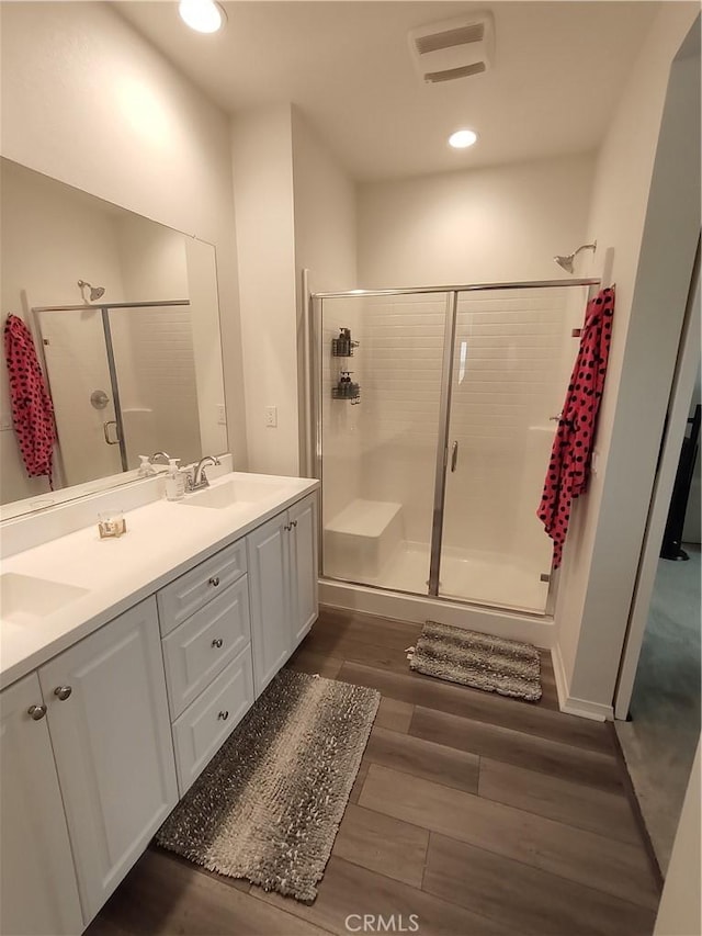 full bathroom with visible vents, a shower stall, double vanity, wood finished floors, and a sink