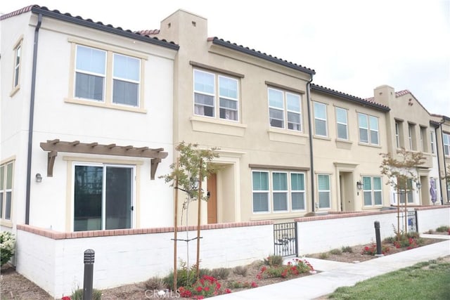 view of front of home with stucco siding, a tile roof, and fence